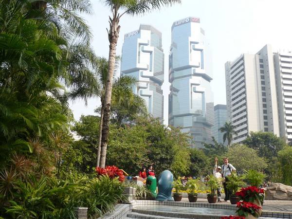 Tourists among palms and flowers in Hong Kong Park, glass Lippo Centre towers behind