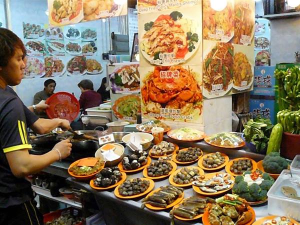 Cook at wok in a night food stall, seafood plates displayed under bright lights