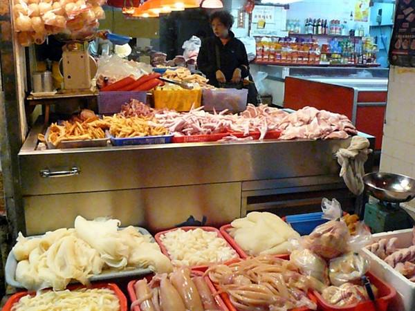Woman behind meat and offal counter in covered market, artificial light