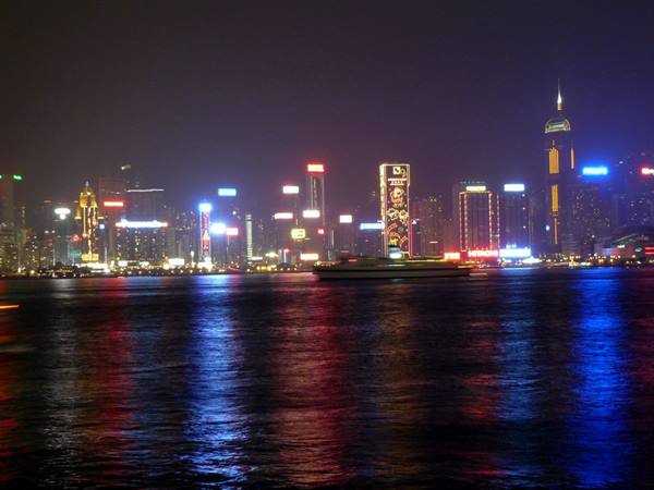 Illuminated skyscrapers at night reflected on the water, a ferry crosses the harbor