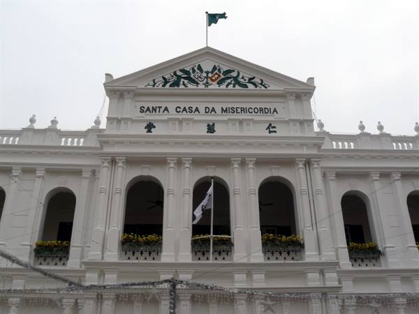 White facade of Santa Casa da Misericórdia in Macau, with arches and yellow flowers