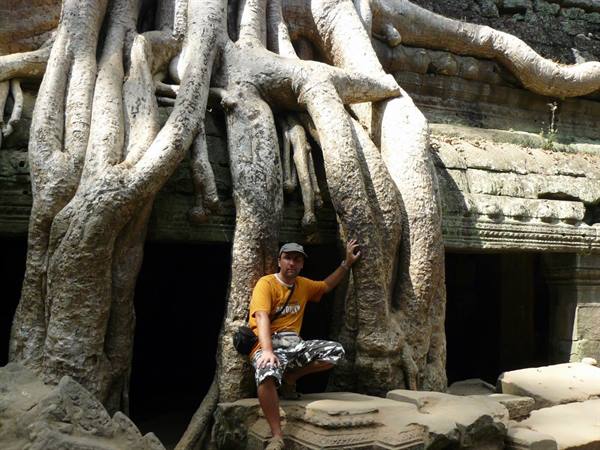 Man crouching among giant tree roots at Ta Prohm temple