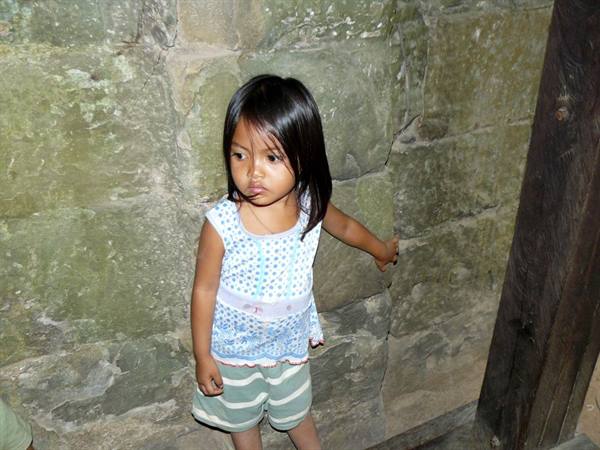 Little girl in blue dress standing beside an ancient stone wall