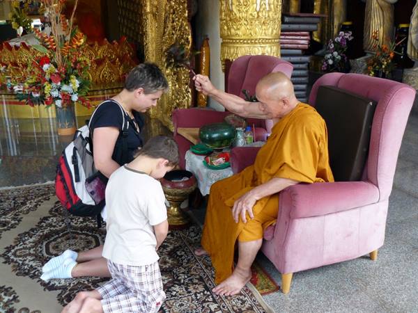 Buddhist monk blesses kneeling mother and child inside the temple