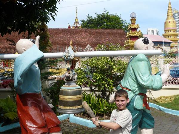Boy with bat between two monk statues carrying a temple bell
