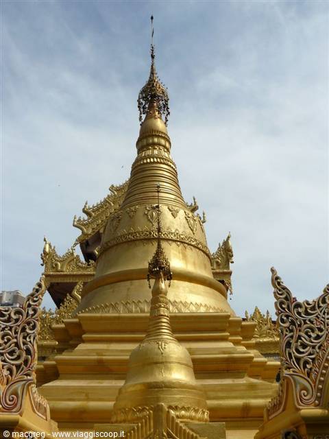 Golden stupa against a cloudy sky, with ornate white pavilions around