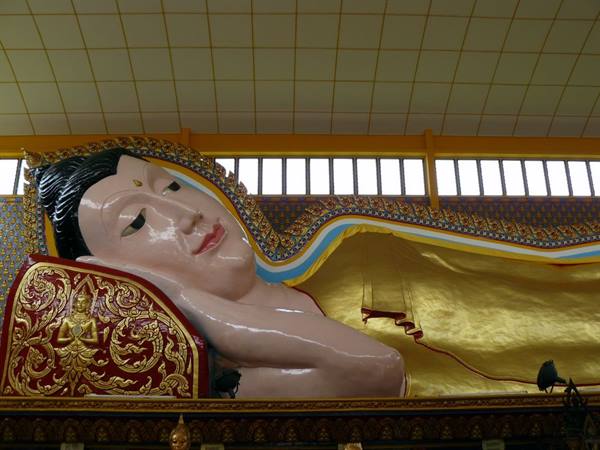 Large golden reclining Buddha inside a Thai temple, window light