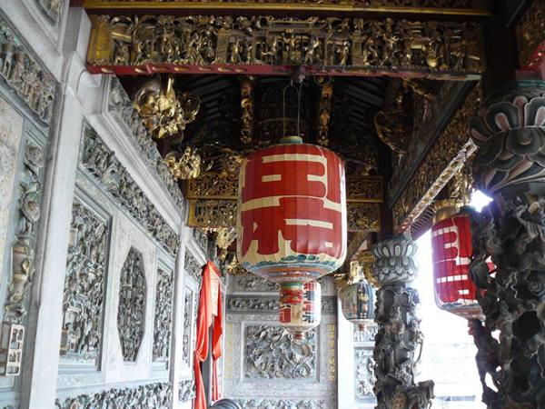 Red lanterns hanging among gilded beams and carved stone at Khoo Kongsi