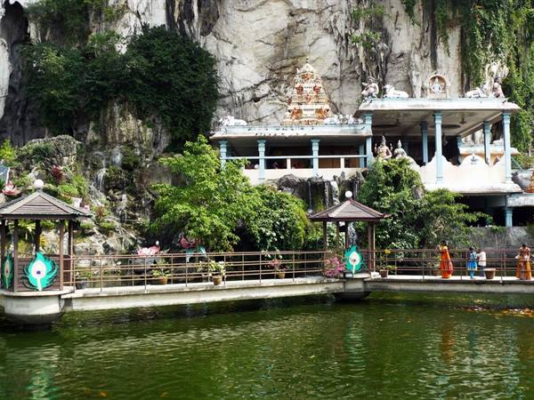 Footbridge over green pond at Batu Caves, Hindu shrine beneath limestone cliff