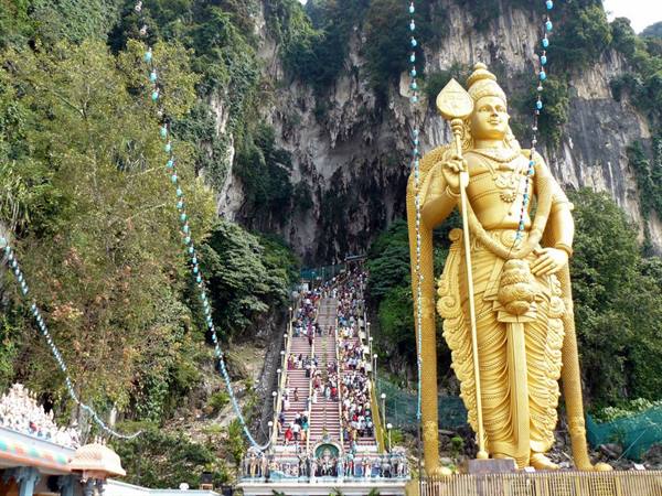 Golden Murugan statue before Batu Caves, crowded staircase climbing the limestone cliff