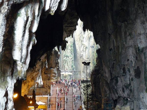 Visitors on the staircase of Batu Caves, natural light through the limestone opening