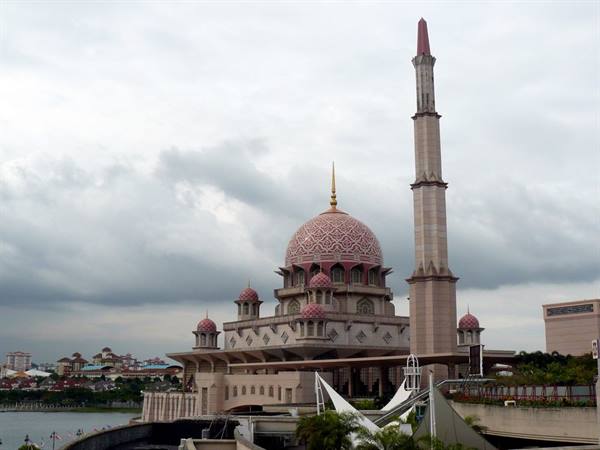 The pink Putra Mosque with minaret by the lake under grey clouds