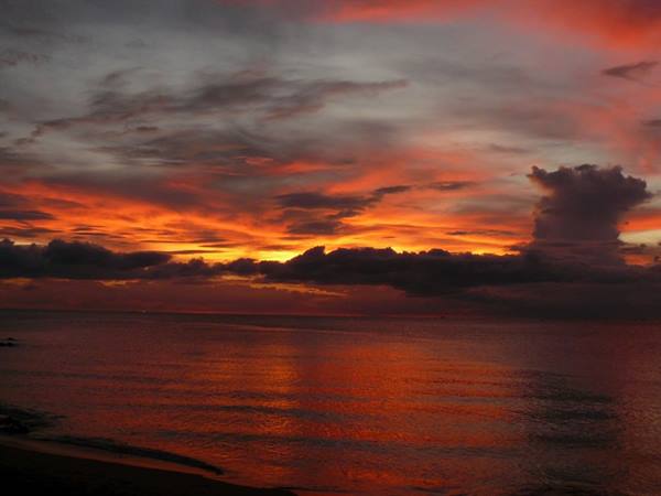 Fiery red and orange clouds reflect over the calm sea by the beach