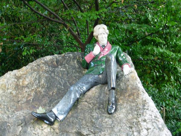 Oscar Wilde statue reclining on a large rock, surrounded by green trees
