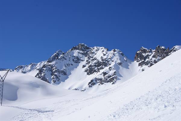 Snow-covered rocky peaks under blue sky, groomed ski slopes on the mountain
