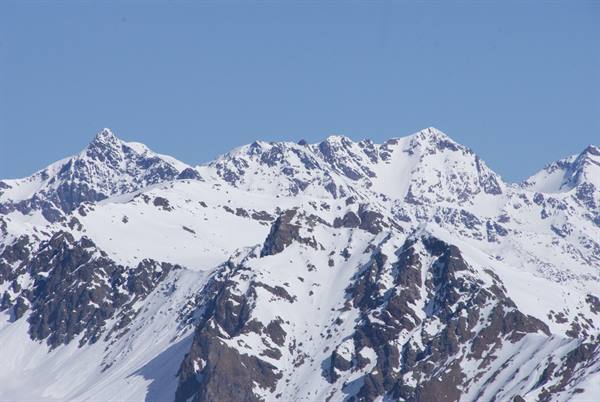 Snow-capped peaks with dark rock outcrops under a clear blue sky