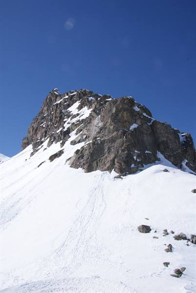 Snow-dusted rocky peak above a steep snowy slope