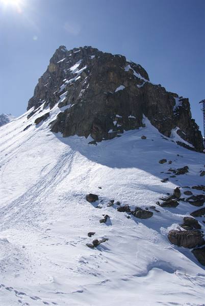 Snow-covered rock outcrop under bright sun, ski tracks at its base