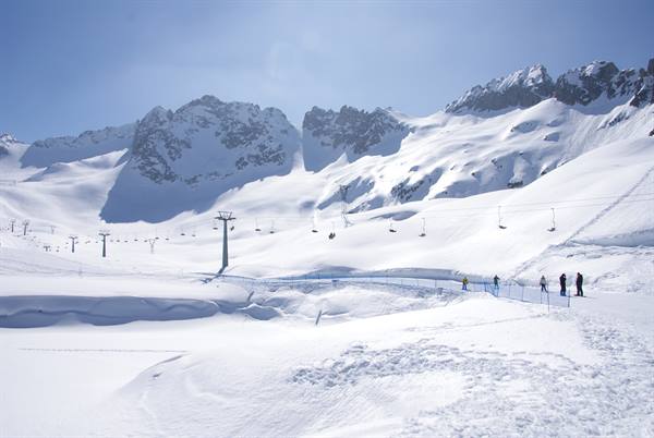 Skiers on pristine snow beneath chairlifts, snow-capped rocky peaks