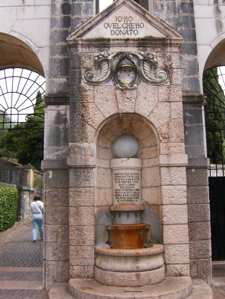 Stone fountain with bronze basin and inscription beneath an archway