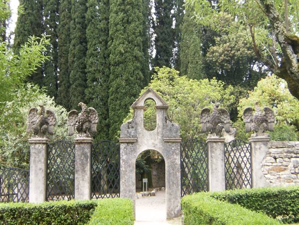 Wrought iron gate topped by carved stone eagles among cypress trees