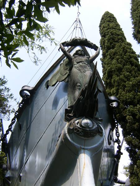 Bronze winged figure on the bow of ship Puglia, Vittoriale, cypress trees