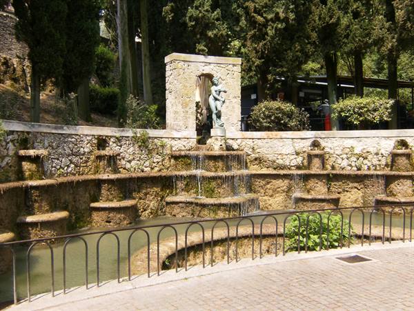Stone cascade fountain with bronze statue, cypress trees, iron railing in front