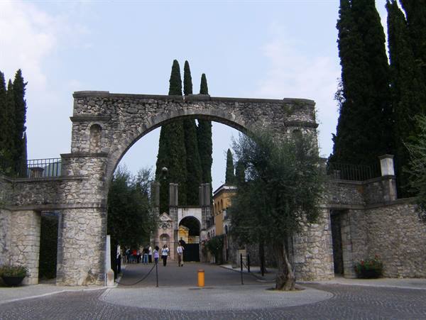 Stone arch entrance of the Vittoriale degli Italiani, tourists under the cypresses