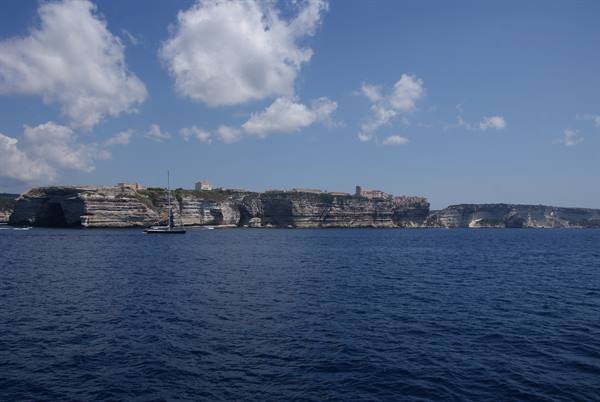 Sailboat in front of Bonifacio limestone cliffs under white clouds