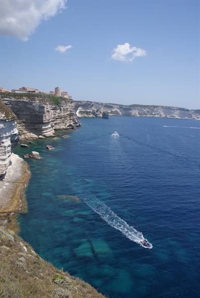 Boat near Bonifacio's white limestone cliffs, turquoise water, village on top