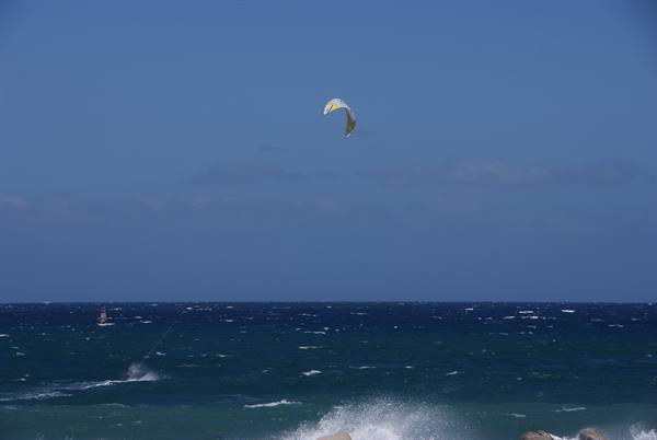 Kitesurfer with yellow kite gliding over blue sea under clear sky