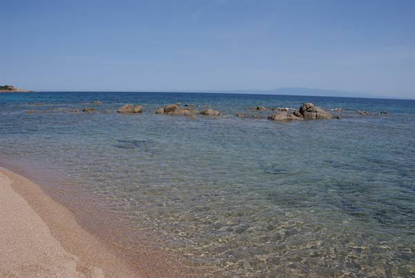 Light sand and granite rocks in clear shallow water, blue sky