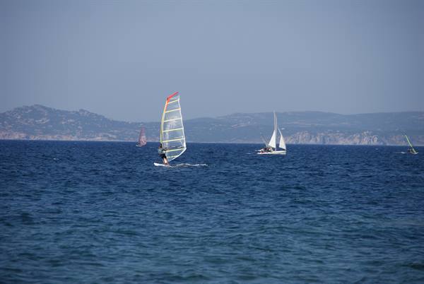 Windsurfer and sailboat on blue sea, hazy hills in background