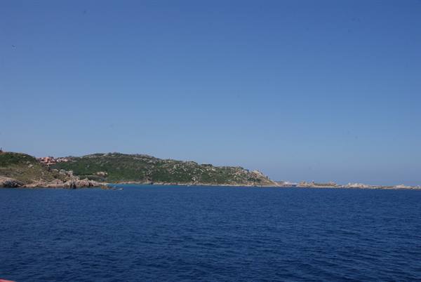 Green granite coastline in deep blue sea under clear sky, houses among Mediterranean scrub