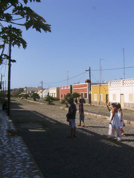 Tourists walk on a paved street among colorful low houses