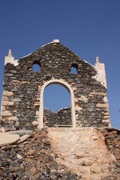 Ruined stone church with white arch, black rocks, blue sky, sunlight