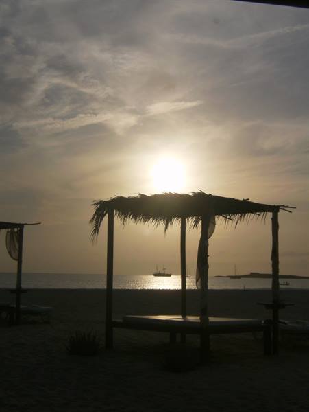 Straw beach gazebo silhouetted against low sun reflecting on the sea