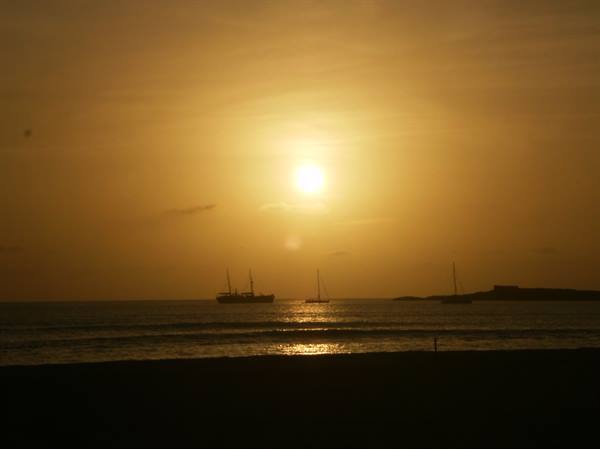Ships and sailboats silhouetted on the golden sea from the beach