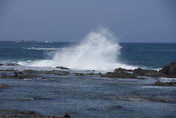 Wave crashing on black rocks, white spray over the blue sea