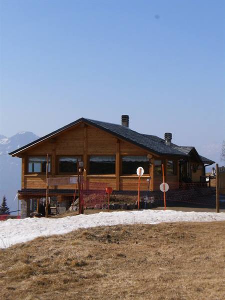 Wooden mountain hut on alpine meadow with leftover snow and ski signs