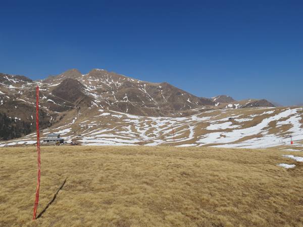Snowy mountain above dry grass field with red pole under blue sky