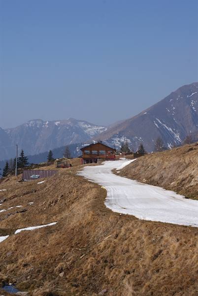Snowy road leading to wooden chalet among bare mountains under blue sky