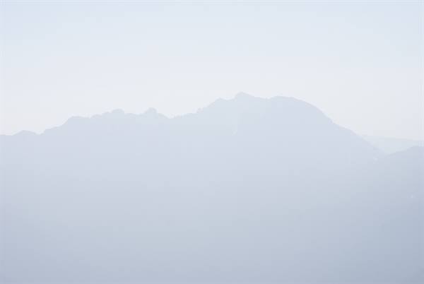 Mountain ridges fading into thick haze, barely visible against pale sky