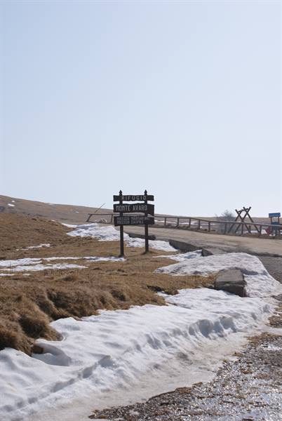 Wooden sign at Colle Croce di Campomaggio, snow along the roadside