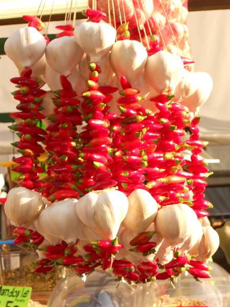 Strings of red chili peppers and white garlic hanging at a market stall