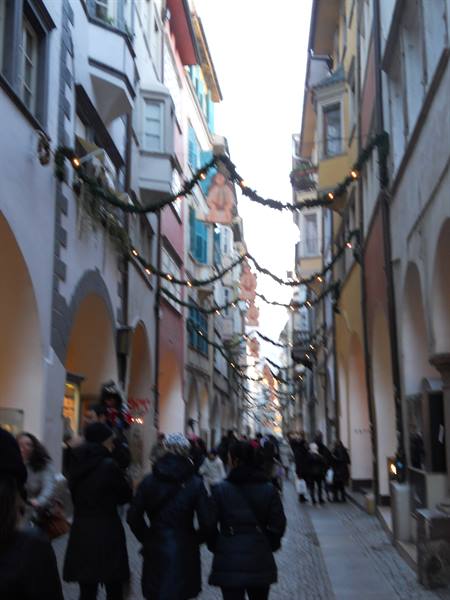 People in coats walk beneath arcades decorated with Christmas garlands