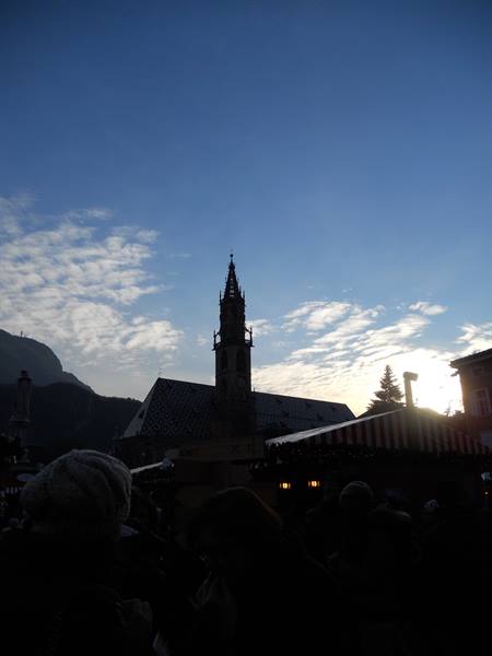 Gothic bell tower of Bolzano Cathedral at dusk among Christmas market stalls
