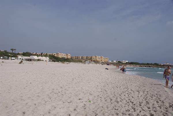White sand beach with bathers, ochre hotels and overcast sky