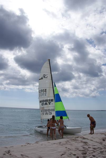 Tourists push a Hobie Cat sailboat onto the sandy beach under cloudy skies