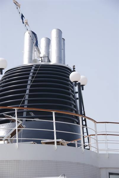 Black ribbed cruise ship funnel with silver exhausts against pale sky